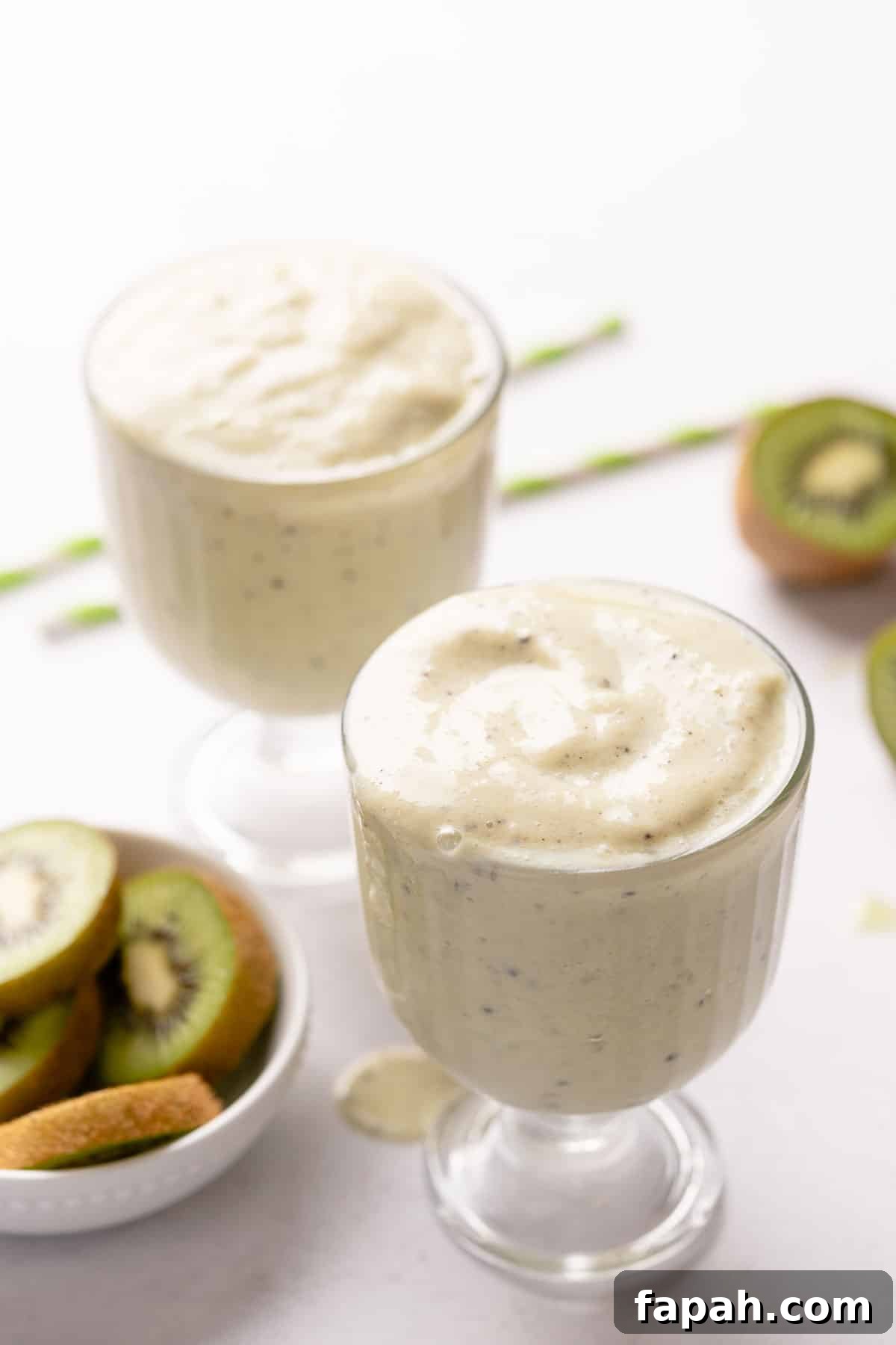 two glasses of smoothie with straws and kiwi on the side