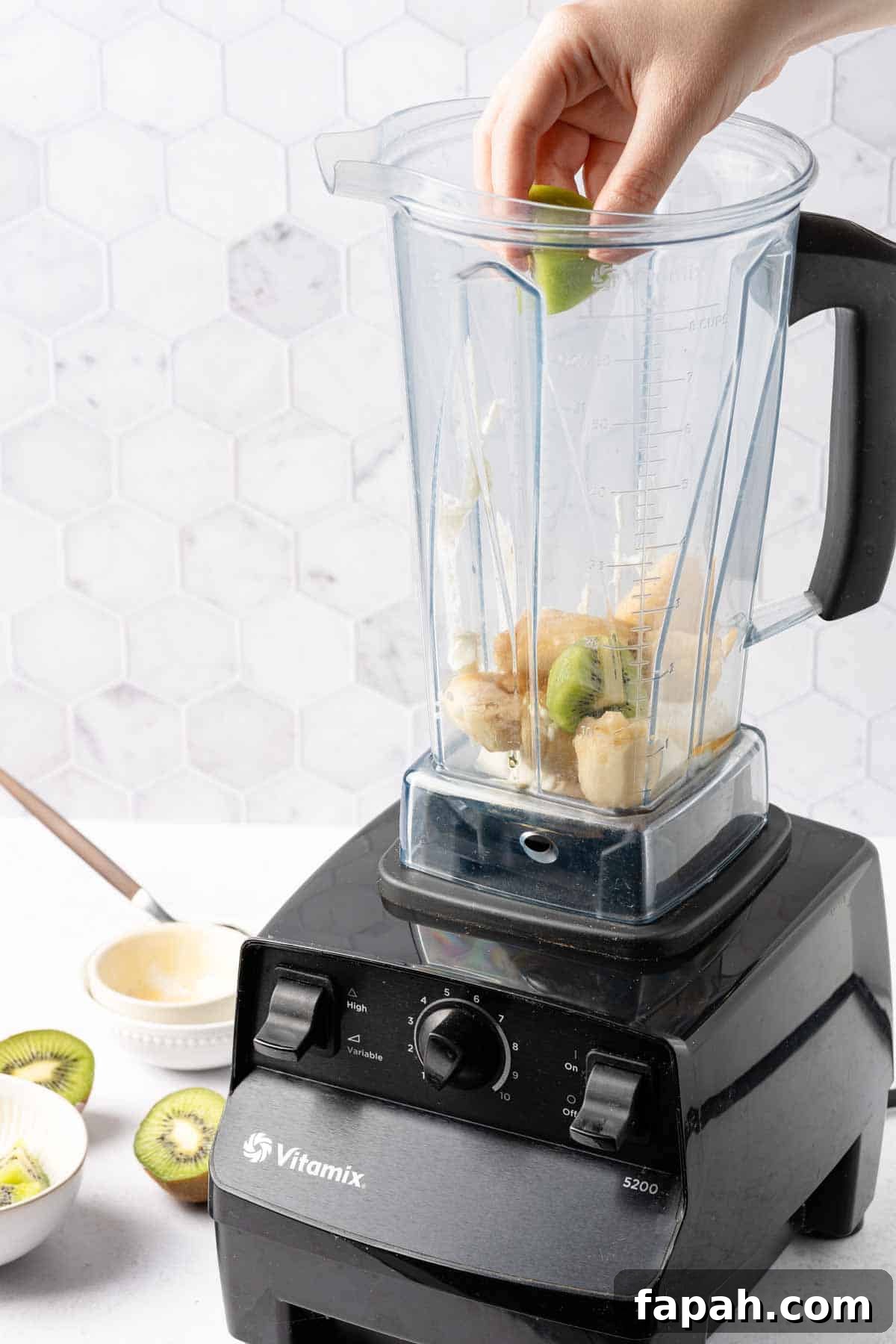 kiwi being added to blender with yogurt and banana inside