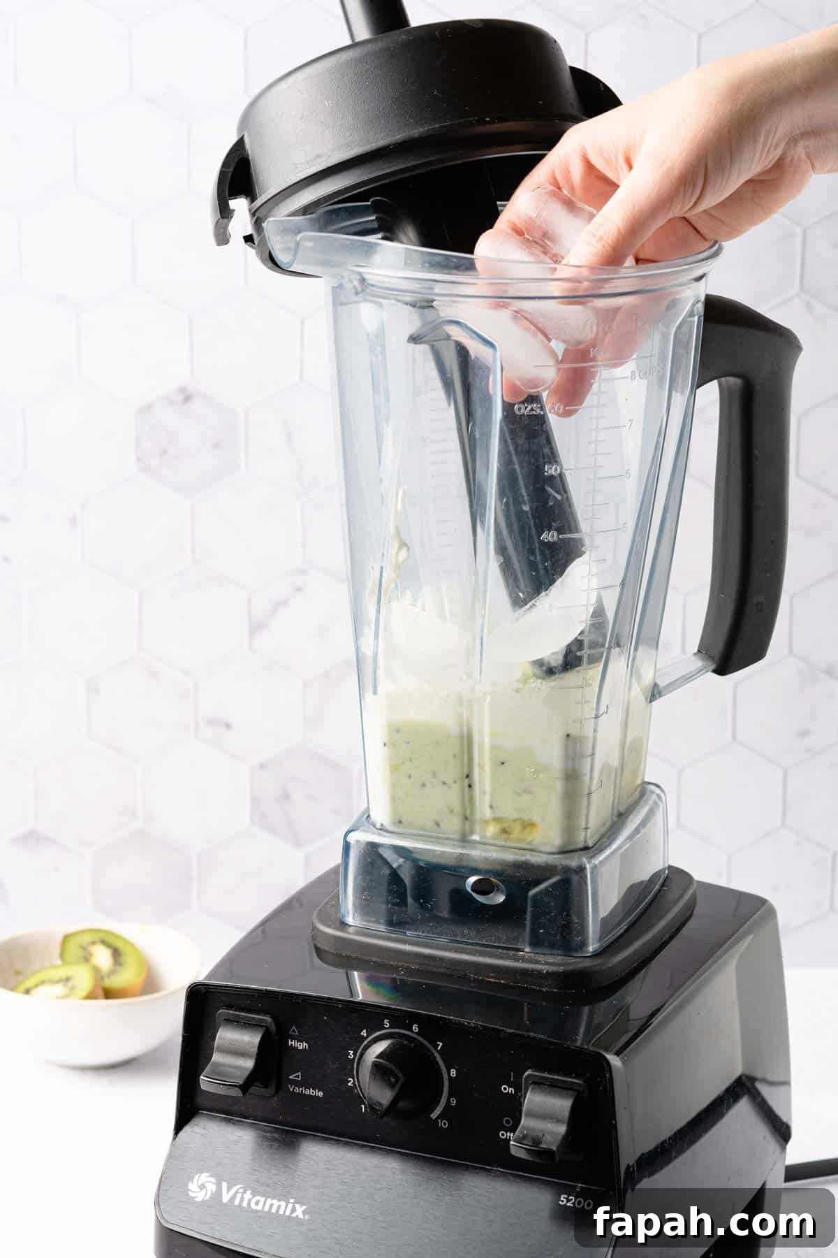 ice being added to blender with blended kiwi banana and yogurt inside