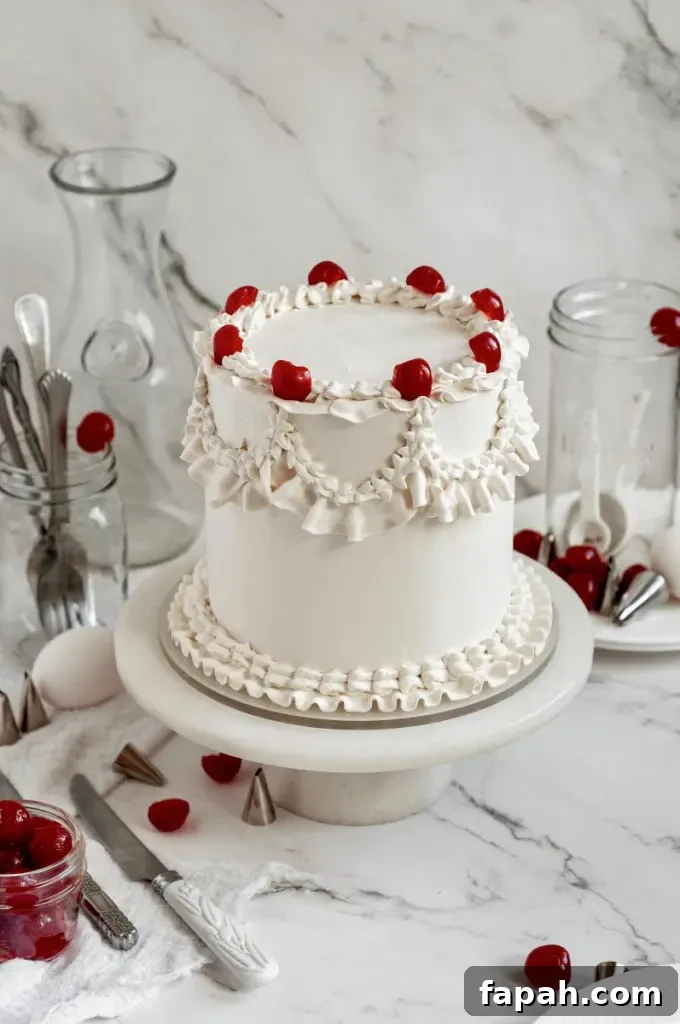 A cherry chip cake with bright white frosting decorated with vintage piping and topped with bright red maraschino cherries.