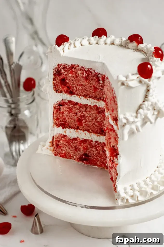 A cherry chip cake with bright white frosting decorated with vintage piping and topped with bright red maraschino cherries.
