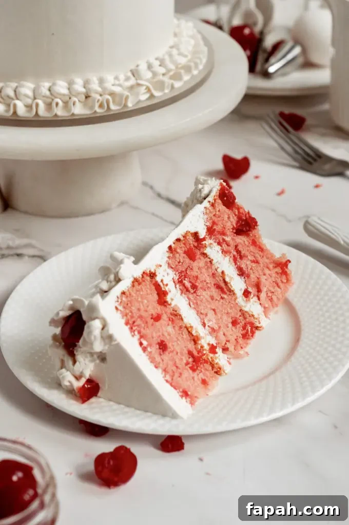 A cherry chip cake with bright white frosting decorated with vintage piping and topped with bright red maraschino cherries.