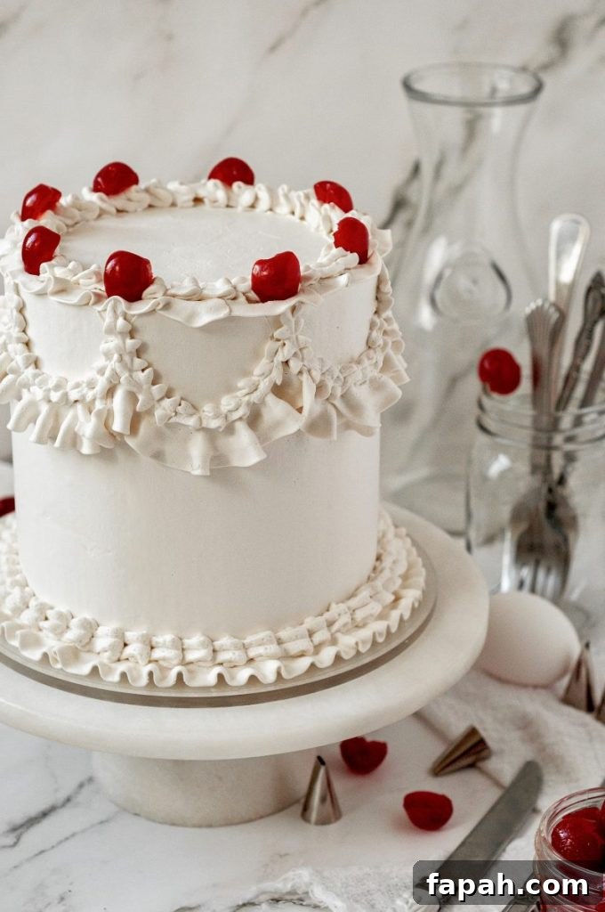 A cherry chip cake with bright white frosting decorated with vintage piping and topped with bright red maraschino cherries.