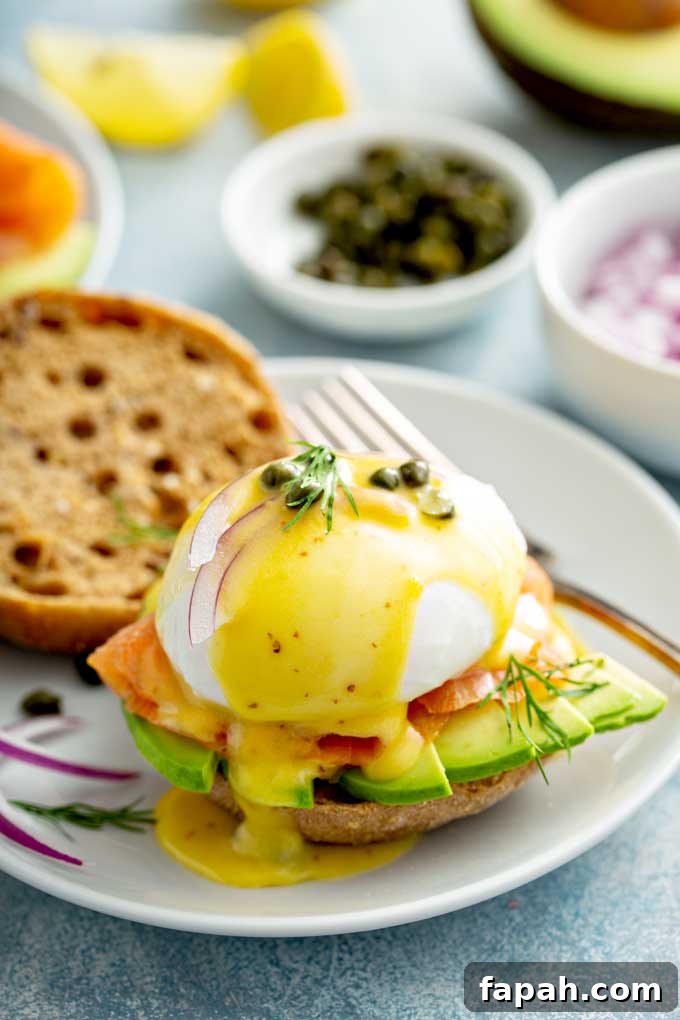 Smoked salmon topped with poached egg and Hollandaise sauce on an English muffin with sliced avocado, onions and capers