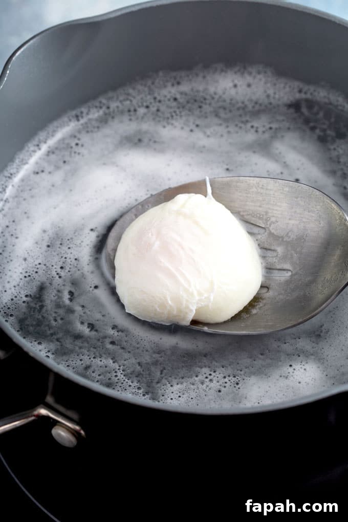A slotted spoon lifting a poached egg from a pot with hot poaching water.