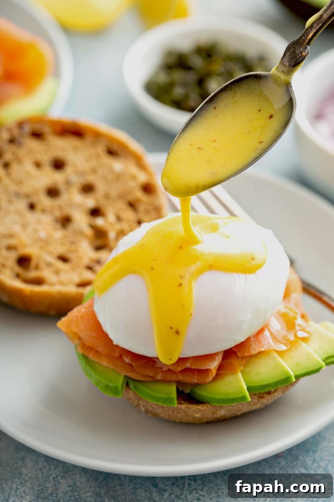 Spoon pouring Hollandaise sauce over Salmon Eggs Benedict.