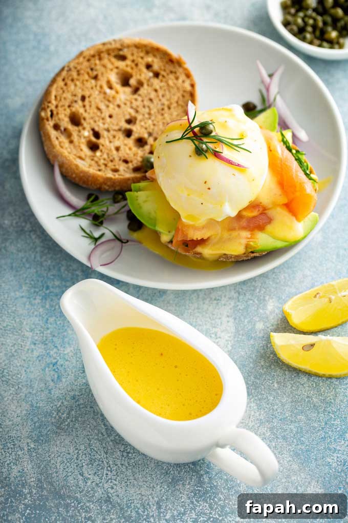 Hollandaise sauce in a white saucer next to a plate with Eggs Benedict.