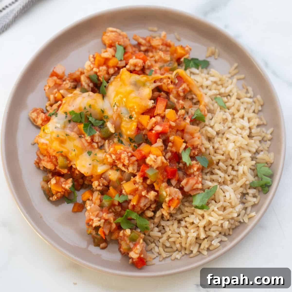 Unstuffed pepper skillet with ground chicken on a white rimmed plate served with brown rice and garnished with fresh parsley.