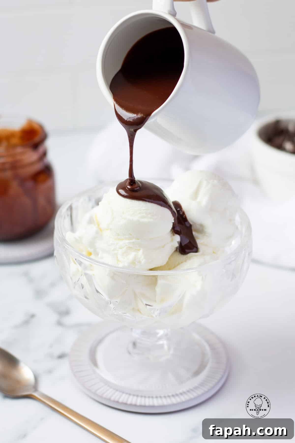 hot fudge in a white pitcher, pouring over a bowl of vanilla ice cream.