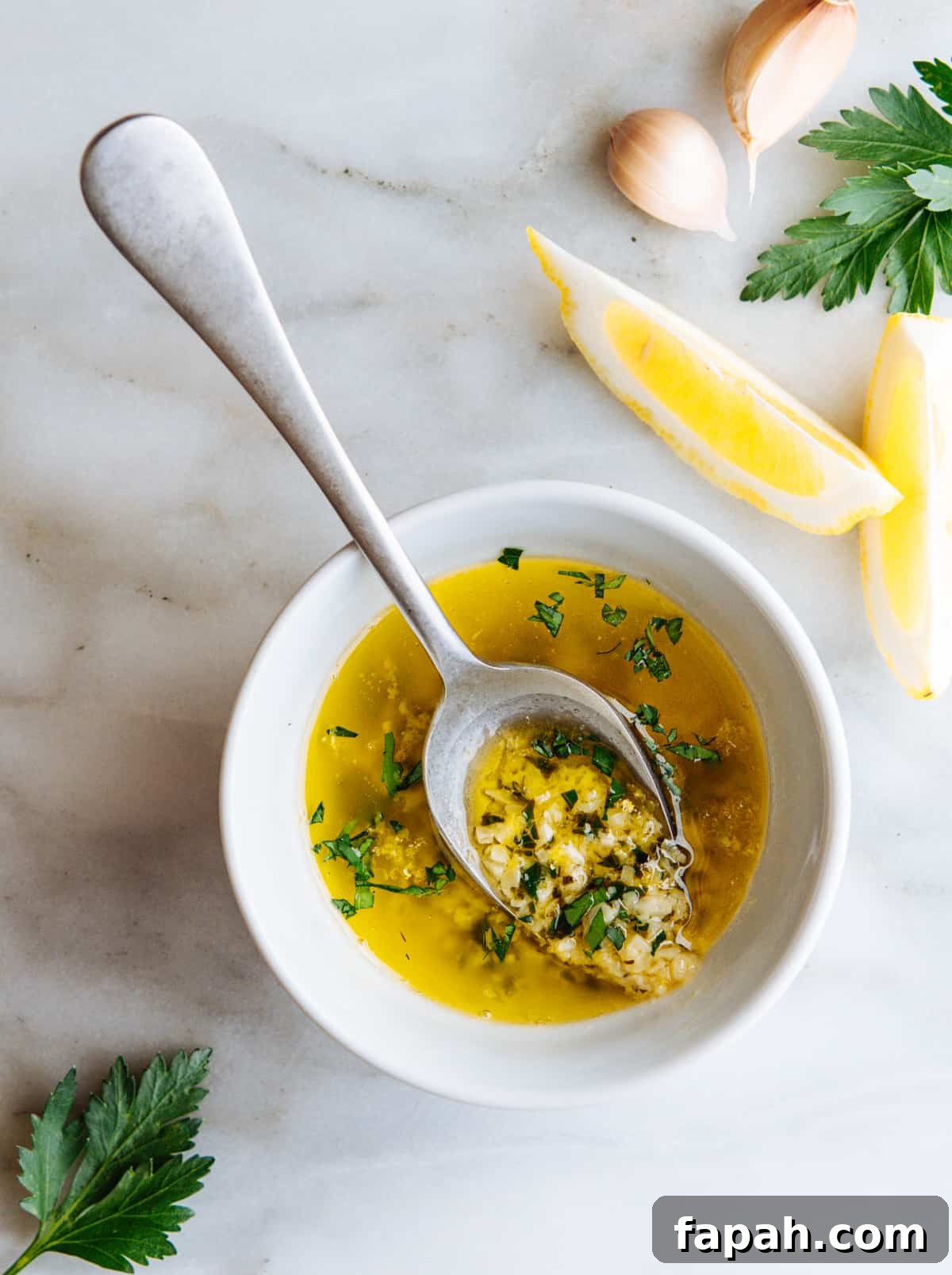 Lemon Garlic Butter Sauce served in a white bowl with a serving spoon on a white marble board