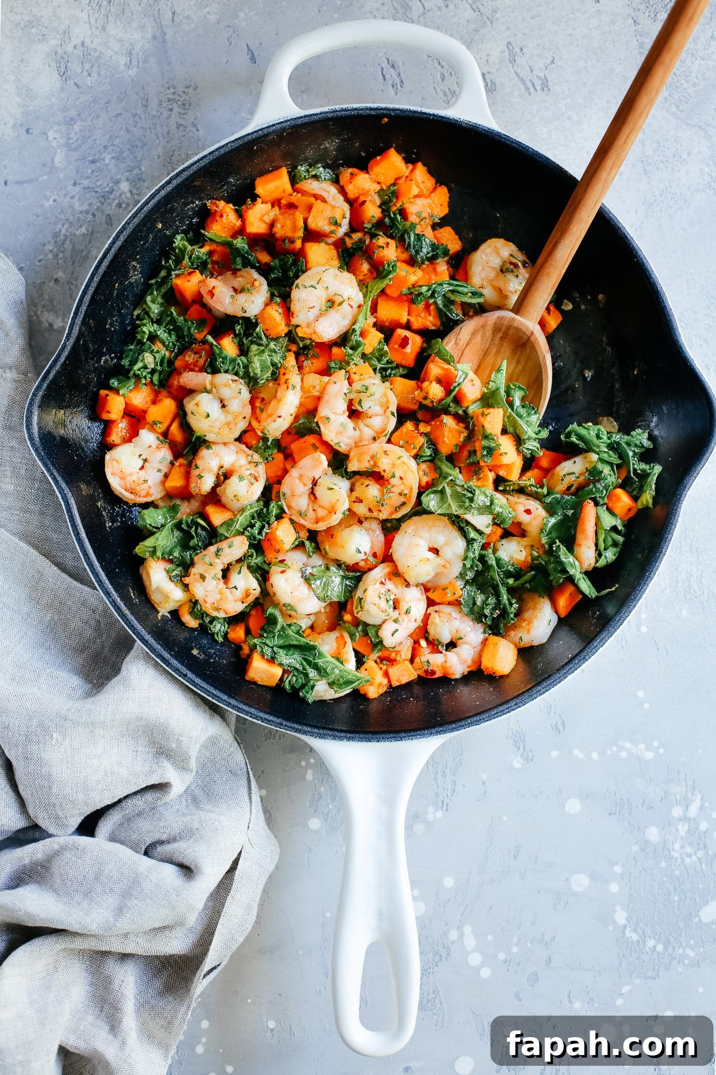60 Delicious Whole30 Recipes for Every Meal and Snack 3 A white skillet with shrimp, kale, and sweet potatoes with a spoon inside.
