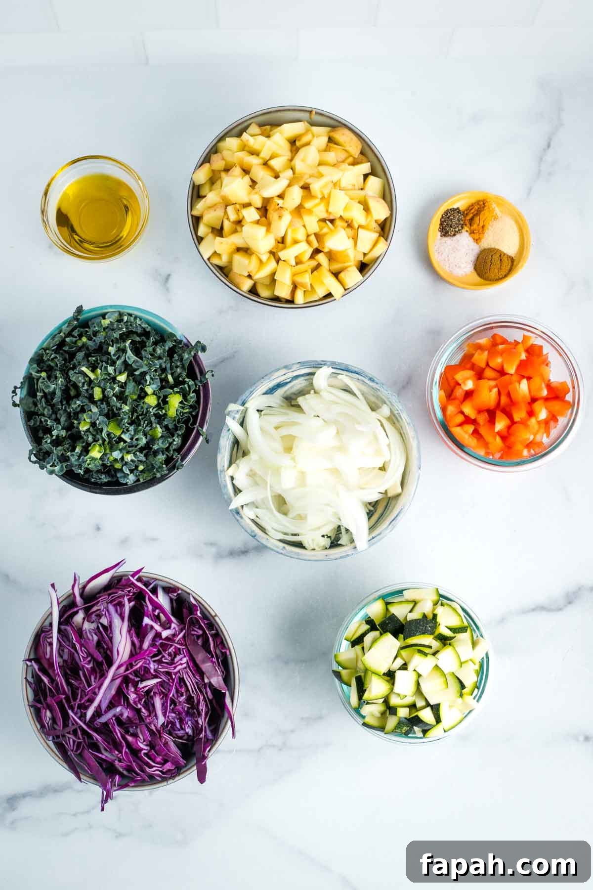 Small bowls with chopped potatoes, bell peppers, onion, cabbage, kale and zucchini. A small dish of olive oil and an assortment of measured spices.