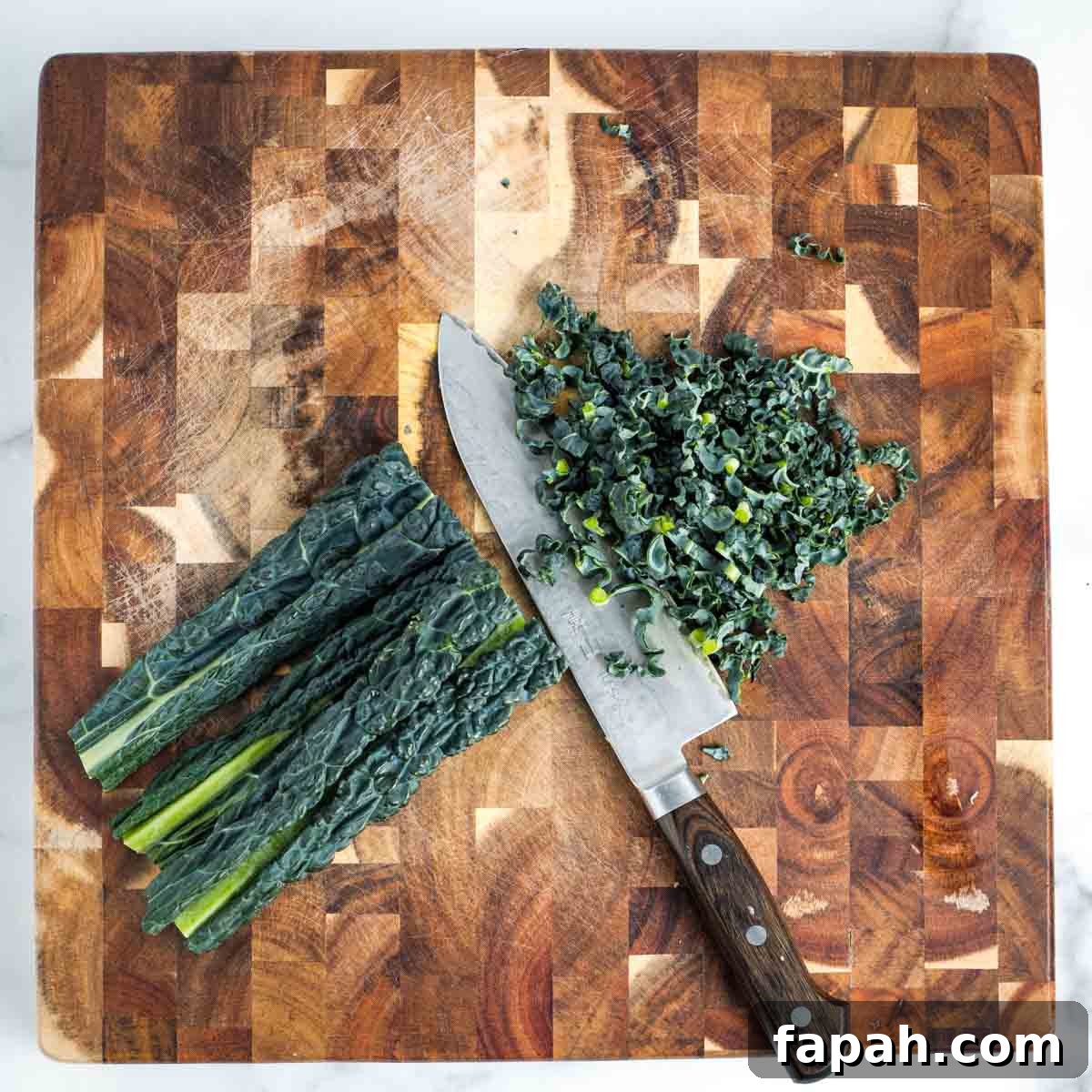 Thinly slicing a stack of lacinato kale on a wooden board.