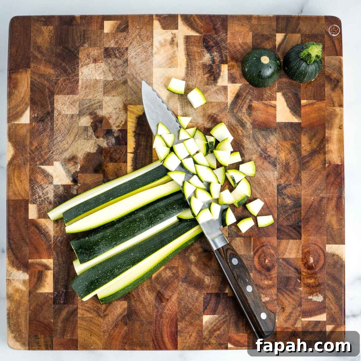 Showing how to dice a zucchini on a wooden cutting board.