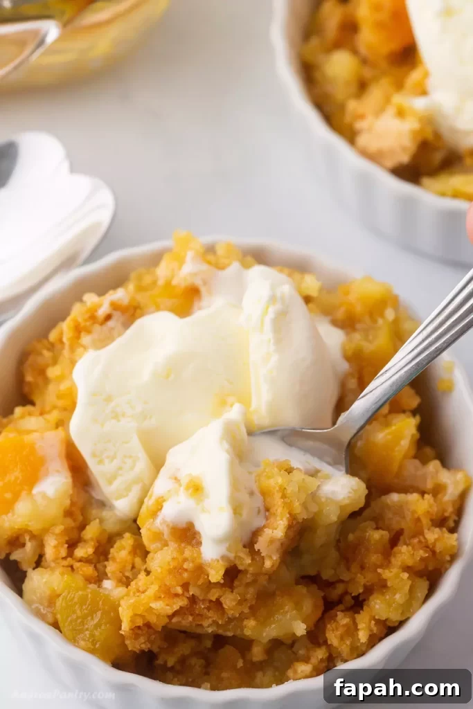 A bowl of peach cobbler with an ice cream scoop on top.