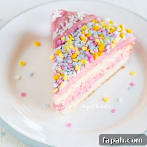Slice of vanilla bean cake frosted with strawberry swiss meringue buttercream and topped with sprinkles on a dessert plate.