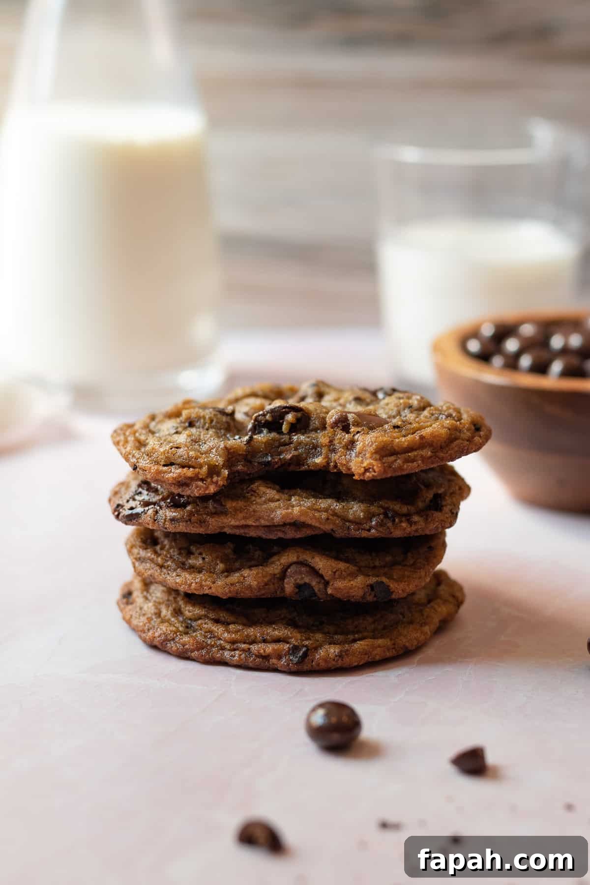 stack of espresso chocolate chip cookies with glasses of milk in the background