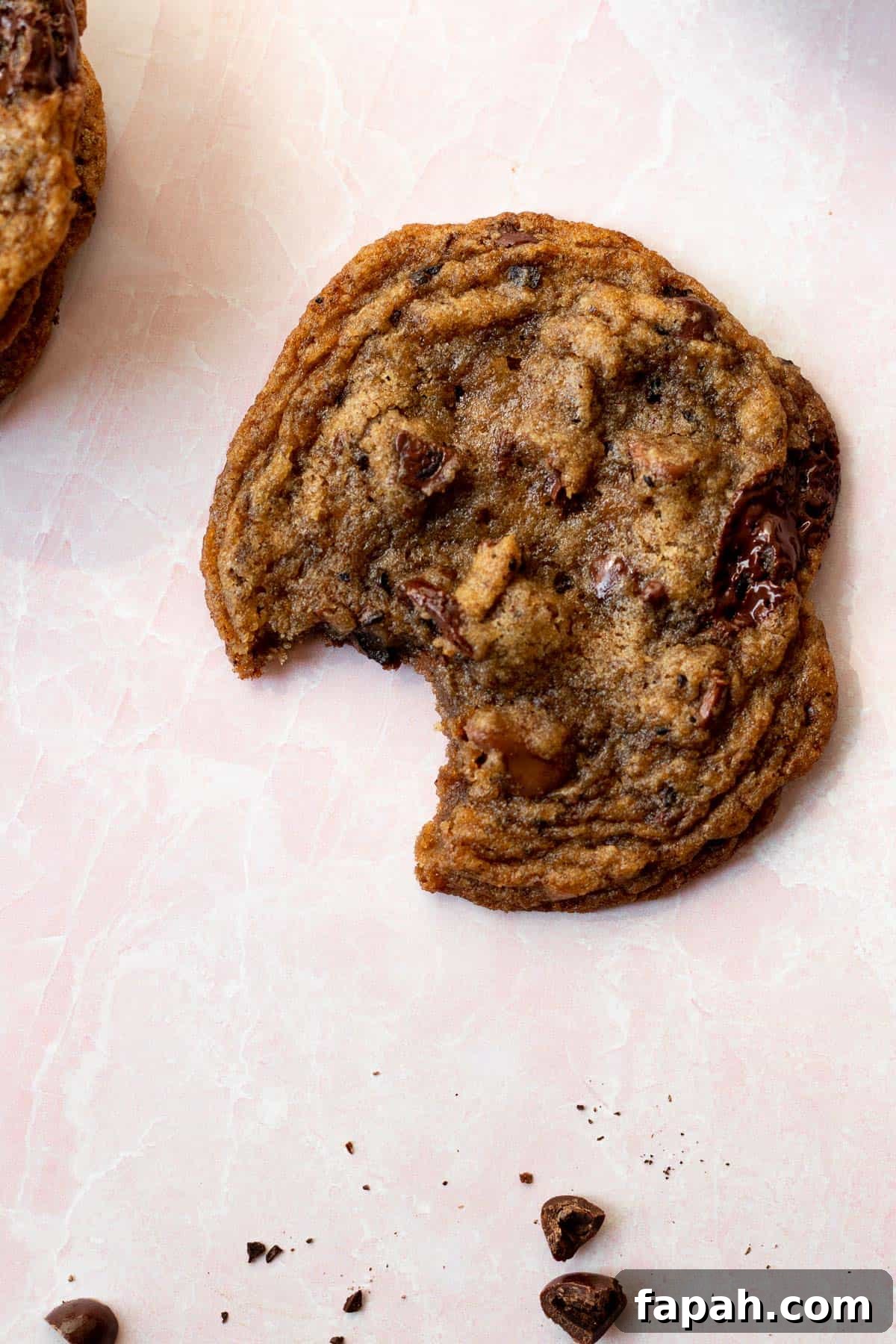 espresso chocolate chip cookie with a bite out of it on a pink background with espresso beans