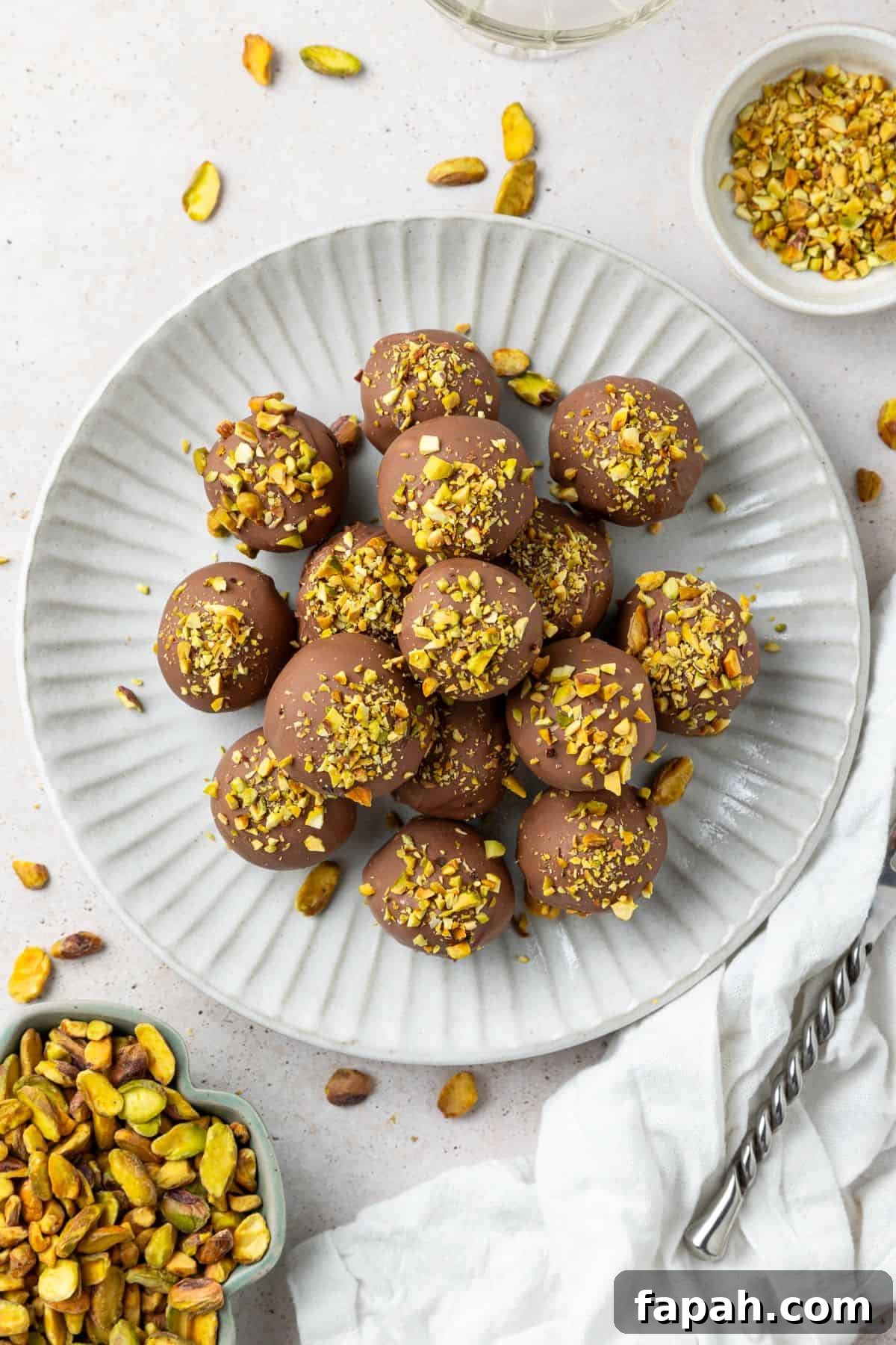 Decadent Pistachio Truffle Recipe — No-Bake Chocolate Pistachios 2 Round grey plate topped with Pistachio Truffles, with some additional pistachios around the edge.