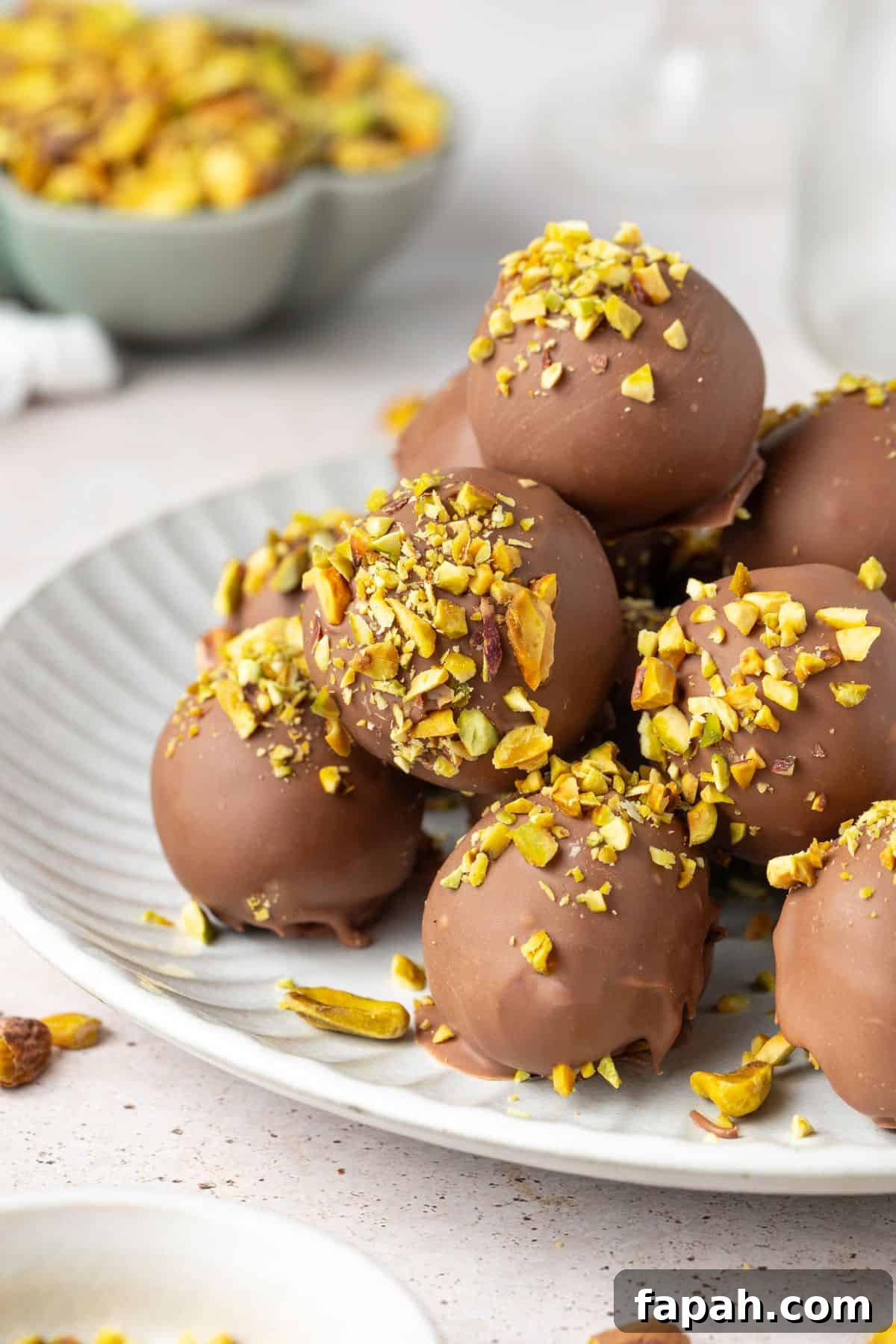 Decadent Pistachio Truffle Recipe — No-Bake Chocolate Pistachios 4 Round grey plate topped with Pistachio Truffles, with some additional pistachios in a bowl on the side.