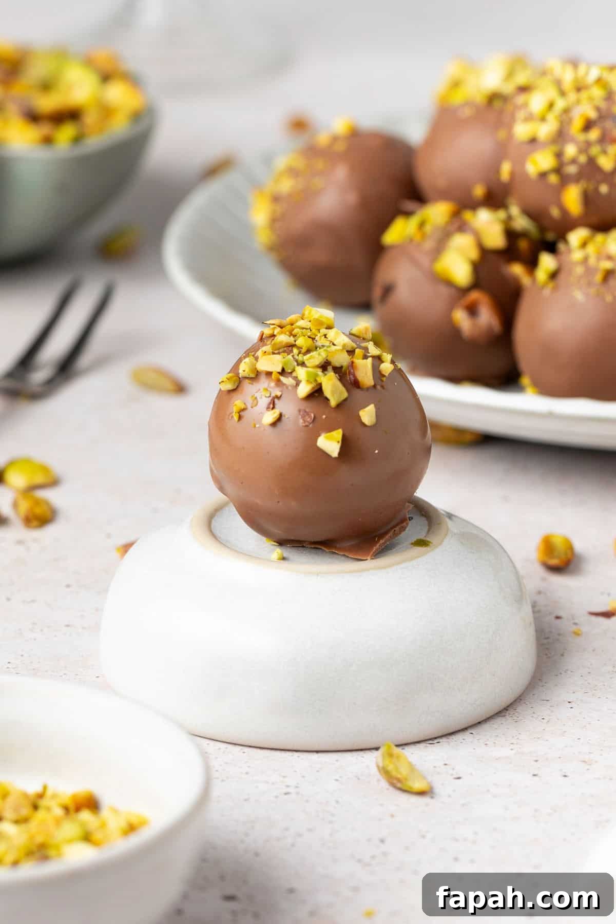 Decadent Pistachio Truffle Recipe — No-Bake Chocolate Pistachios 8 A Pistachio Truffle sitting on a small dish, with a plate of truffles in the background.