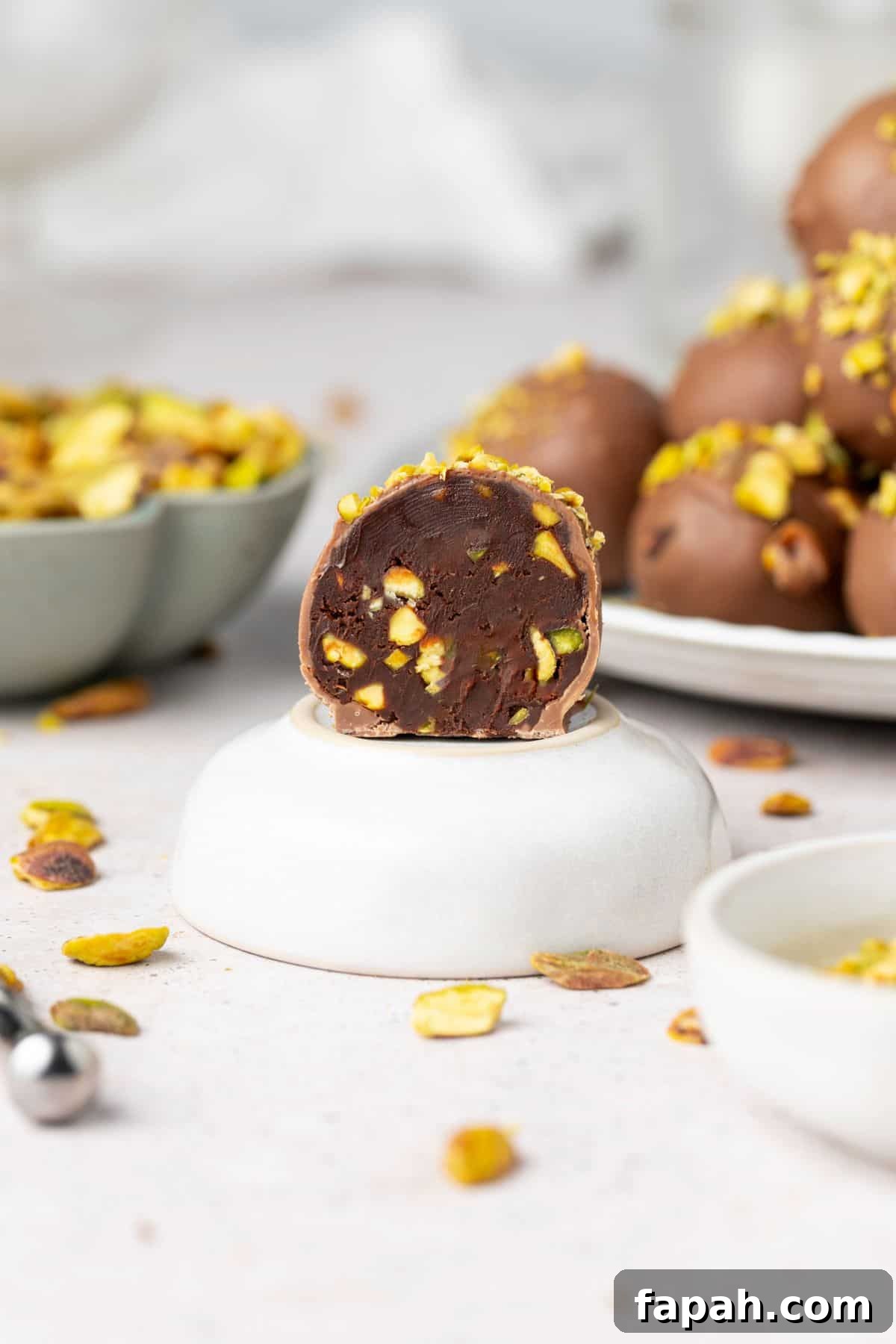 Decadent Pistachio Truffle Recipe — No-Bake Chocolate Pistachios 9 A Pistachio Truffle that has been cut in half, sitting on a small dish, with a plate of truffles in the background.