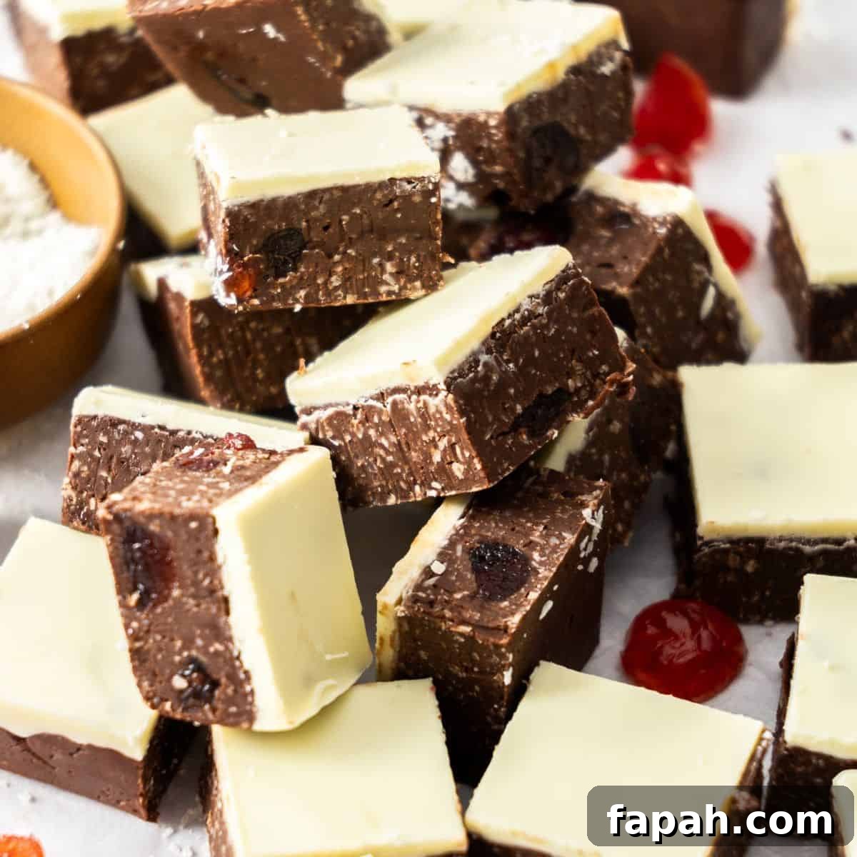 Cut squares of Dark Chocolate Cherry Fudge on some baking paper, with a dish of coconut and some glacé cherries scattered.