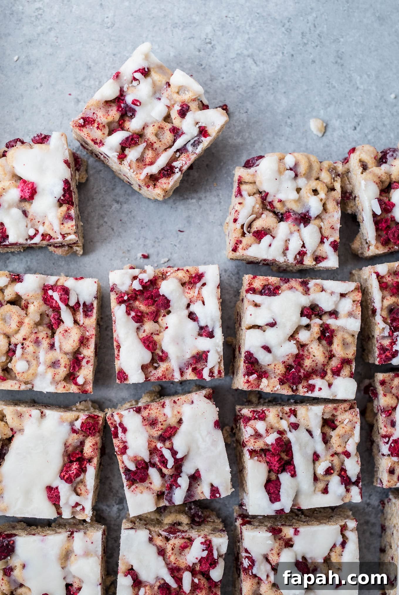 Cereal treats with raspberries and icing on a blue surface.