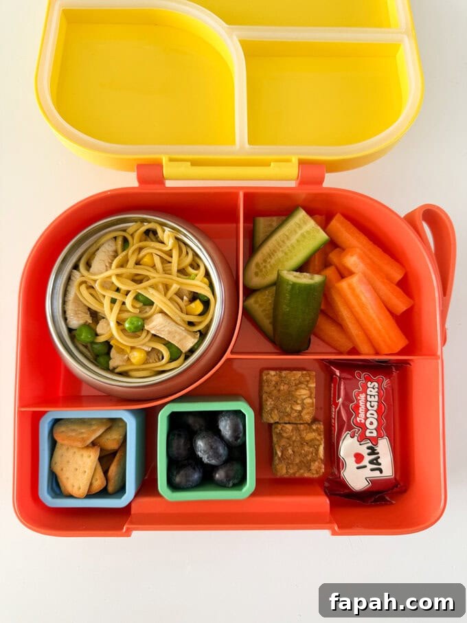 Chicken noodles served in a small kids thermos pot with lid, in a brightly colored multi section lunch box, along with lots of other snacks.