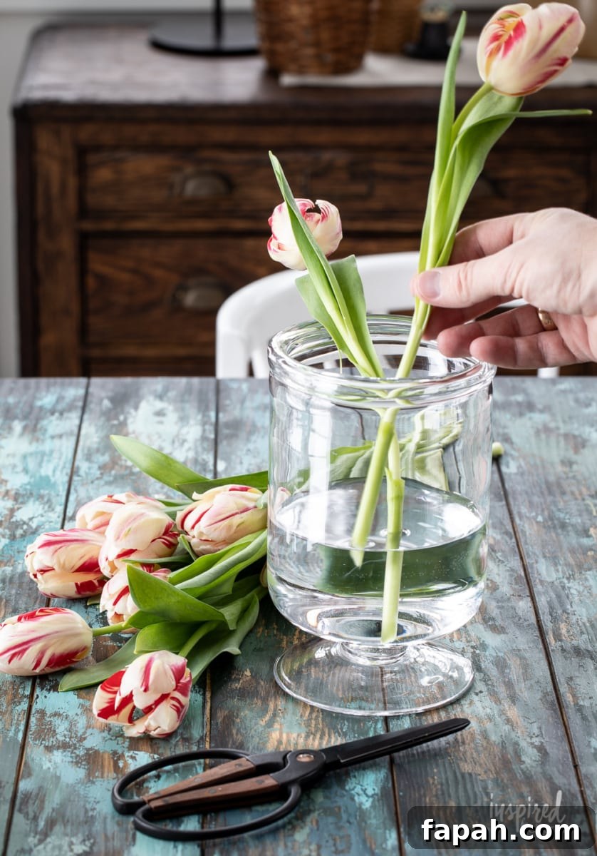 Complete Guide to Flower Arranging: Techniques, Tips & Styles 5 hand arranging tulips in clear glass vase.
