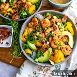 Grey bowl with mango, shrimp and salad in it. Cilantro and bacon to the side
