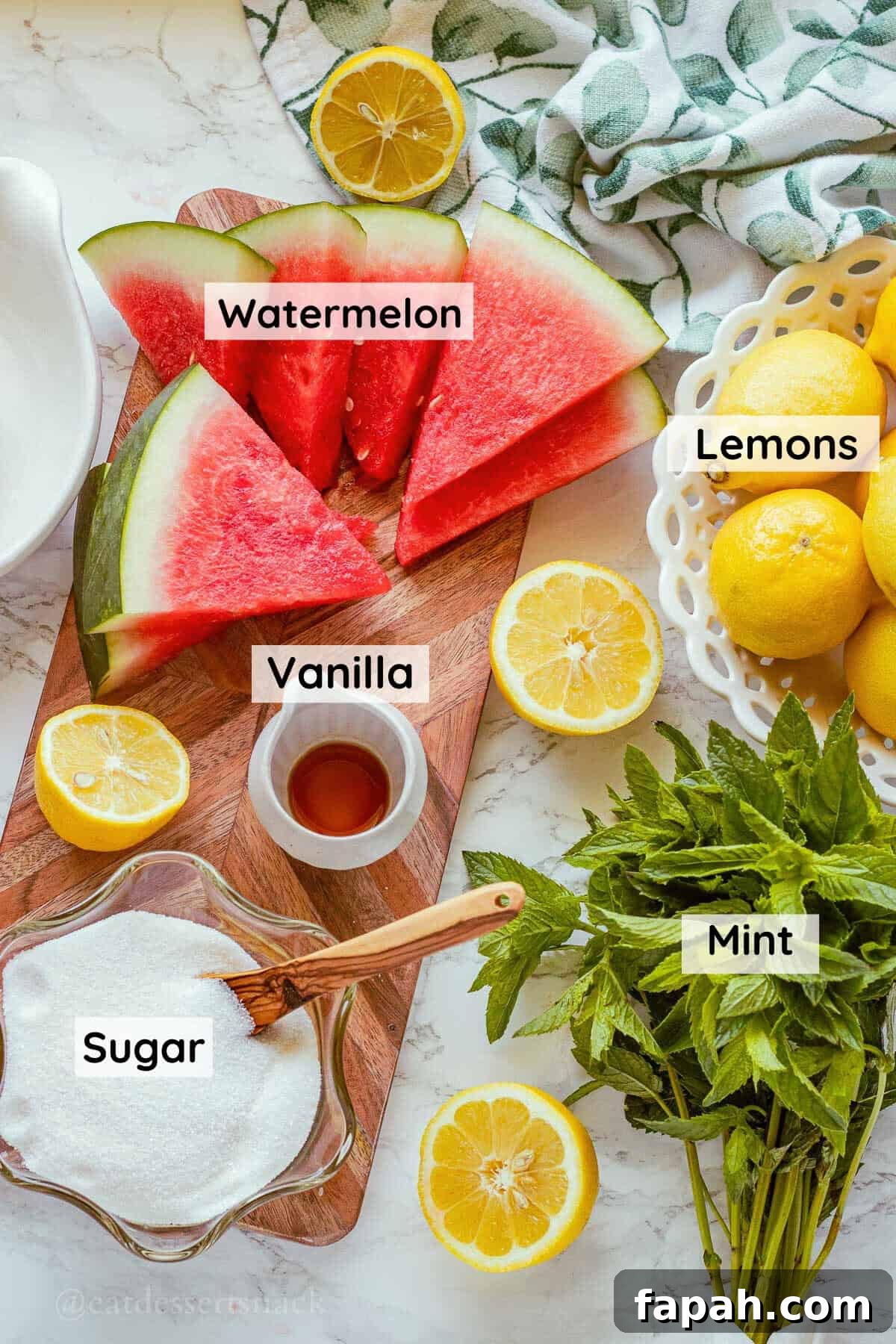 Watermelon, lemons, sugar, mint, and vanilla with wood cutting board on marble.