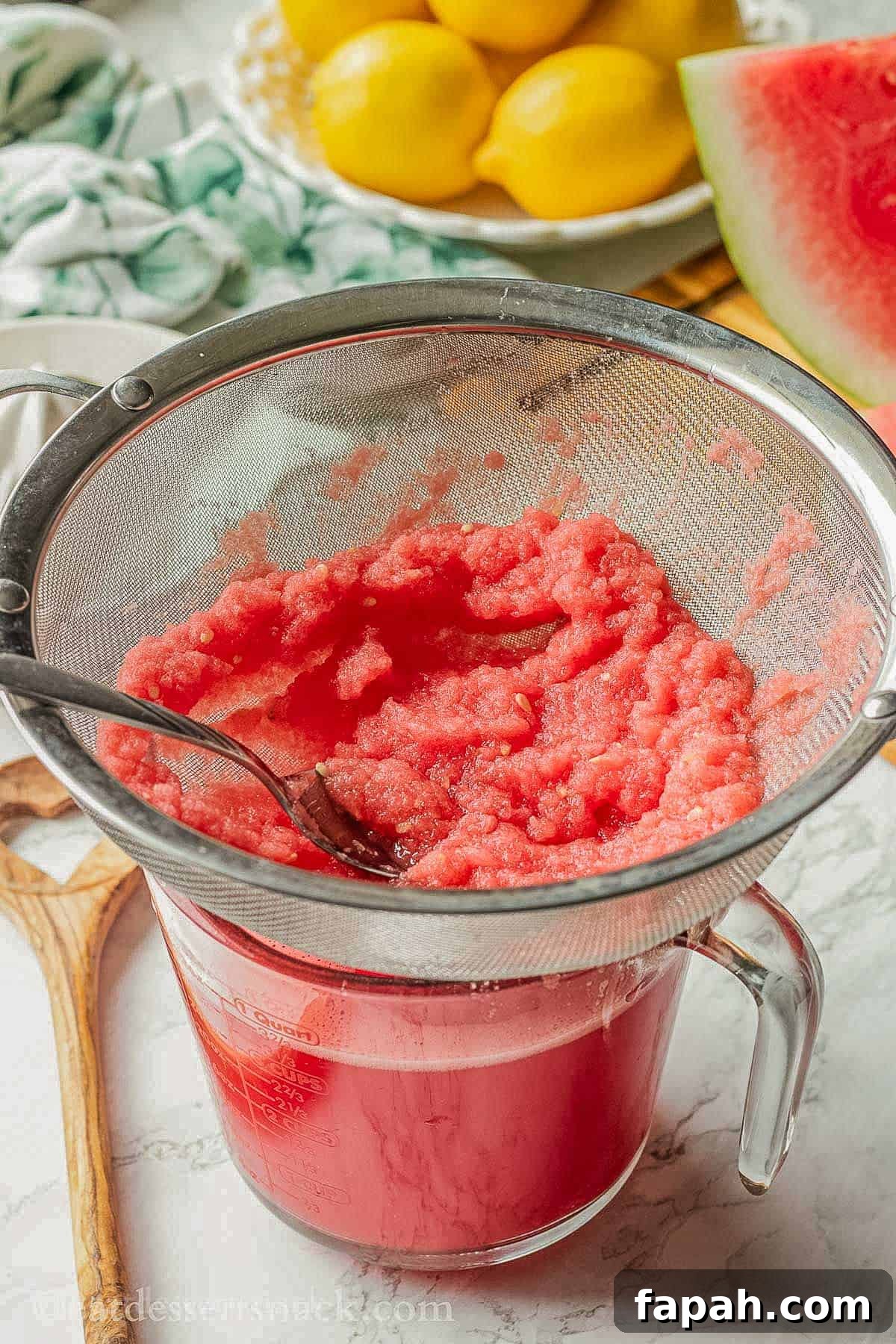 Straining watermelon juice through a sieve into a glass measuring cup.