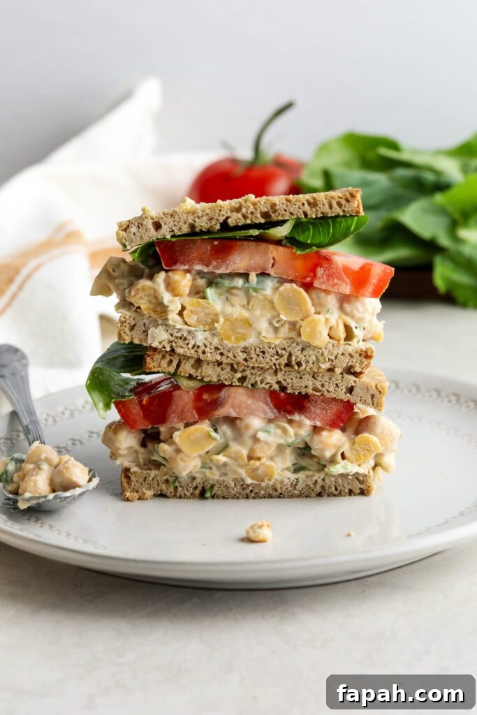 Vegan Chickpea Salad Sandwich stacked on plate with lettuce and tomato in background