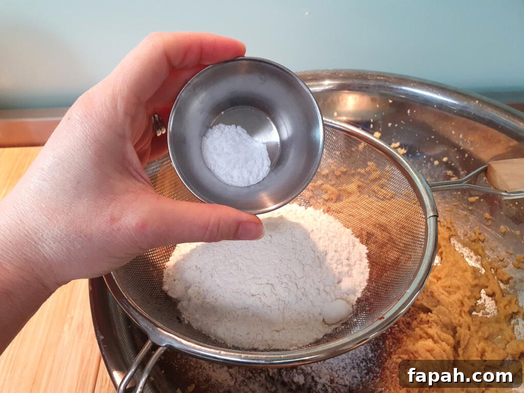 How to Make Homemade Oreo Cookies from Scratch 11 adding baking soda to other dry ingredients in sieve sittnig on top of mixing bowl with beaten wet ingredients.