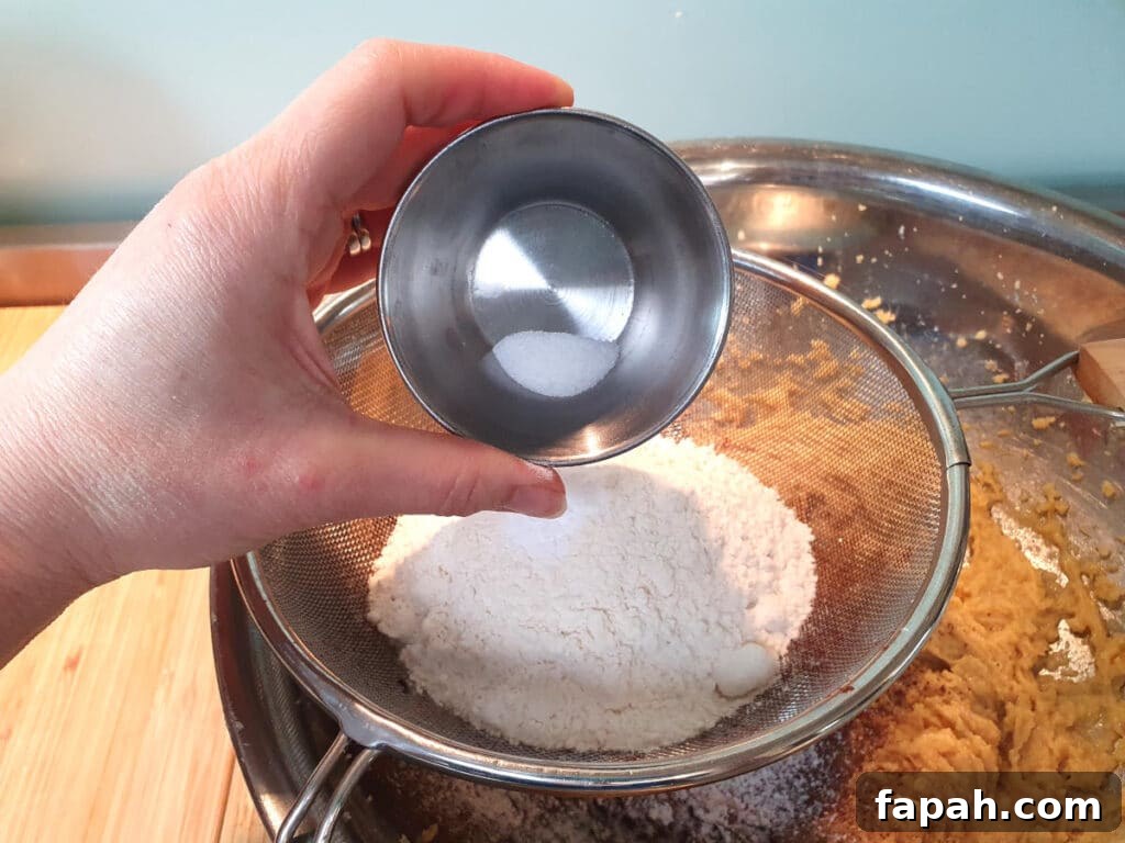 How to Make Homemade Oreo Cookies from Scratch 12 adding salt to other dry ingredients in sieve sittnig on top of mixing bowl with beaten wet ingredients.
