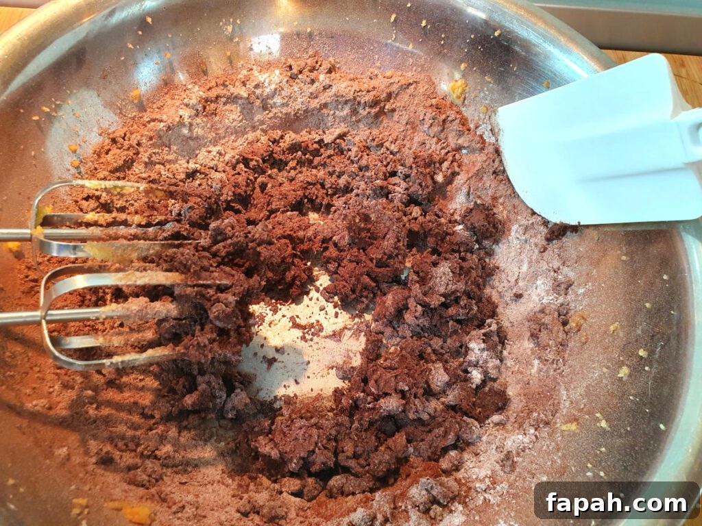 How to Make Homemade Oreo Cookies from Scratch 13 mixing dry ingredients for oreo cookies with beaters to the left and white spatular to the right to scrap down bowl.