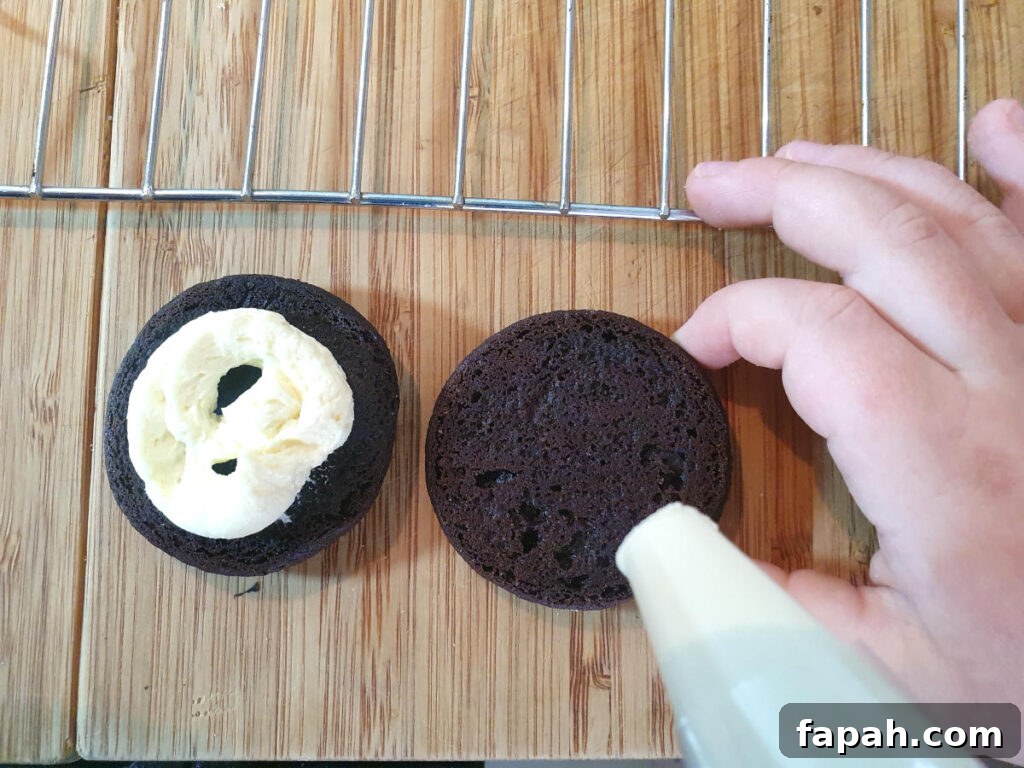 How to Make Homemade Oreo Cookies from Scratch 24 down down view filling oreos with vanilla butter filling in a piping bag.