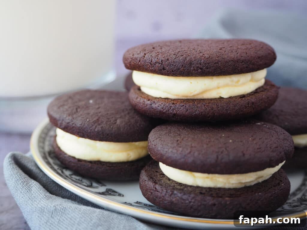 How to Make Homemade Oreo Cookies from Scratch 27 side view of homemade oreas stacked on a a white plate with a black border pattern and gold rim, on a grey tea towel and a glass of milk on the side.