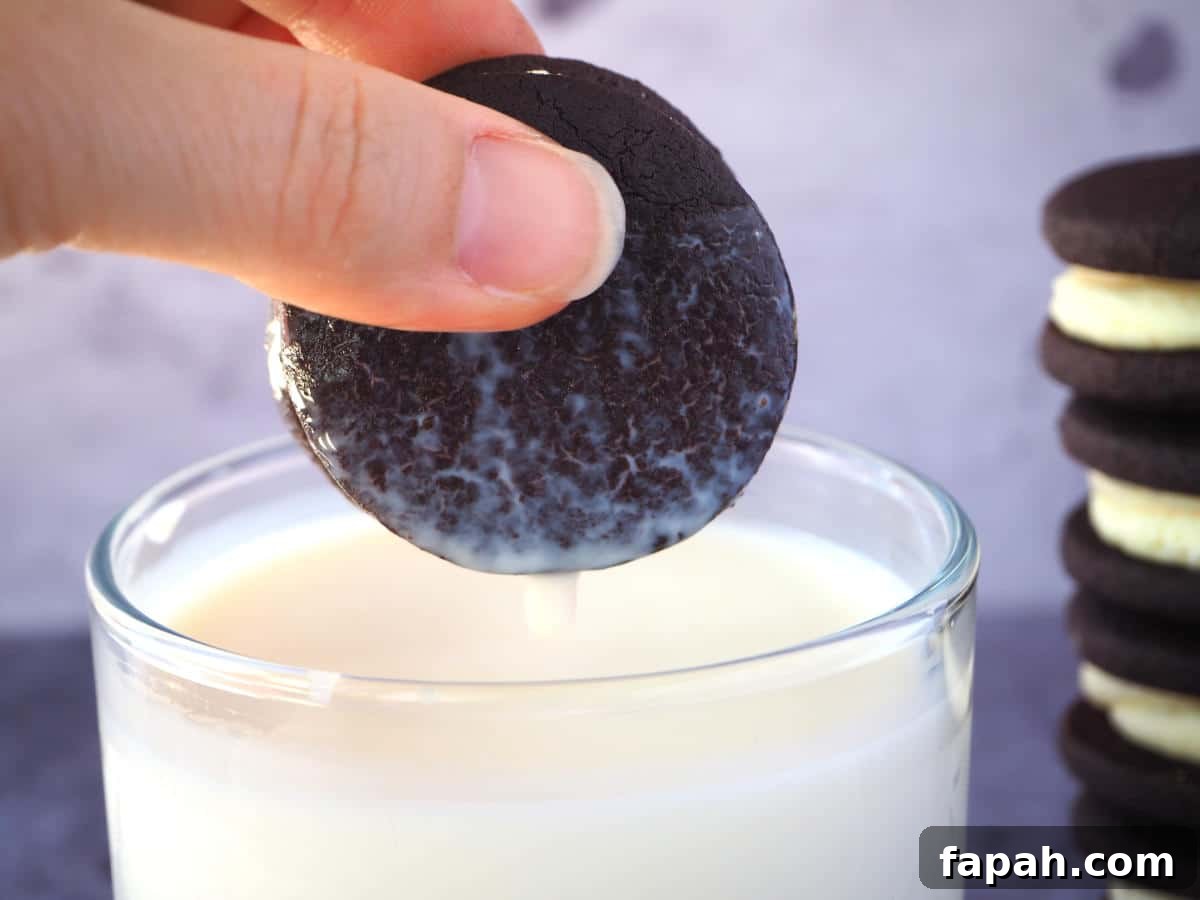How to Make Homemade Oreo Cookies from Scratch 28 side view homemade oreo that's just been dunked in a glass of mil, with milk dripping off it and a stack of oreos to the side.