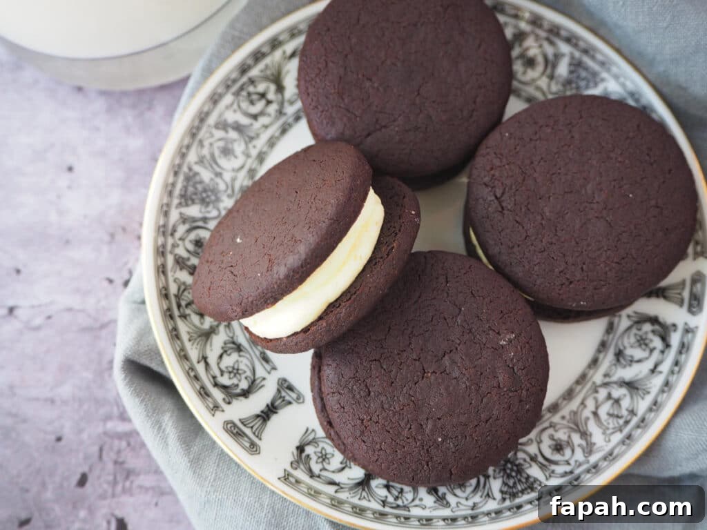 How to Make Homemade Oreo Cookies from Scratch 29 top down view of homemade oreas, with one on its side, on a white plate with a black border pattern and gold rim, on a grey tea towel and a glass of milk on the side.