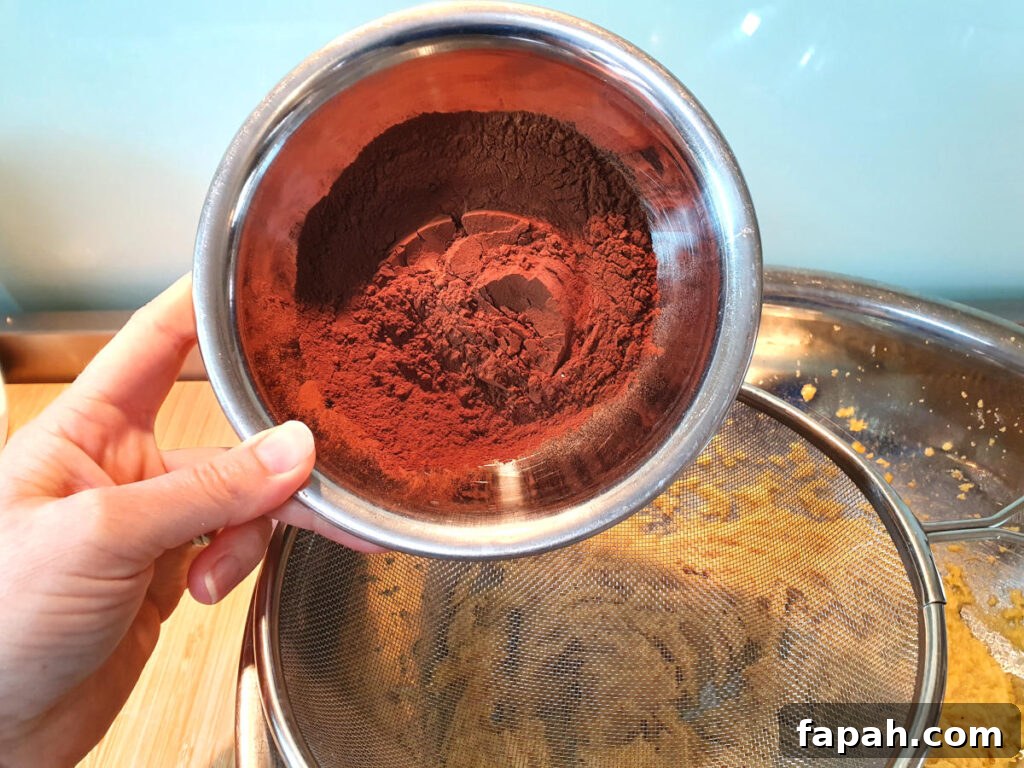 How to Make Homemade Oreo Cookies from Scratch 9 adding dutch cocoa powder to sieve sittnig on top of mixing bowl with beaten wet ingredients.