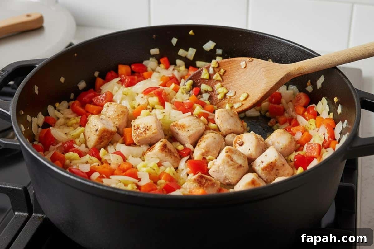 Cooking the onion, garlic, capsicum carrot, and chicken in a pot.