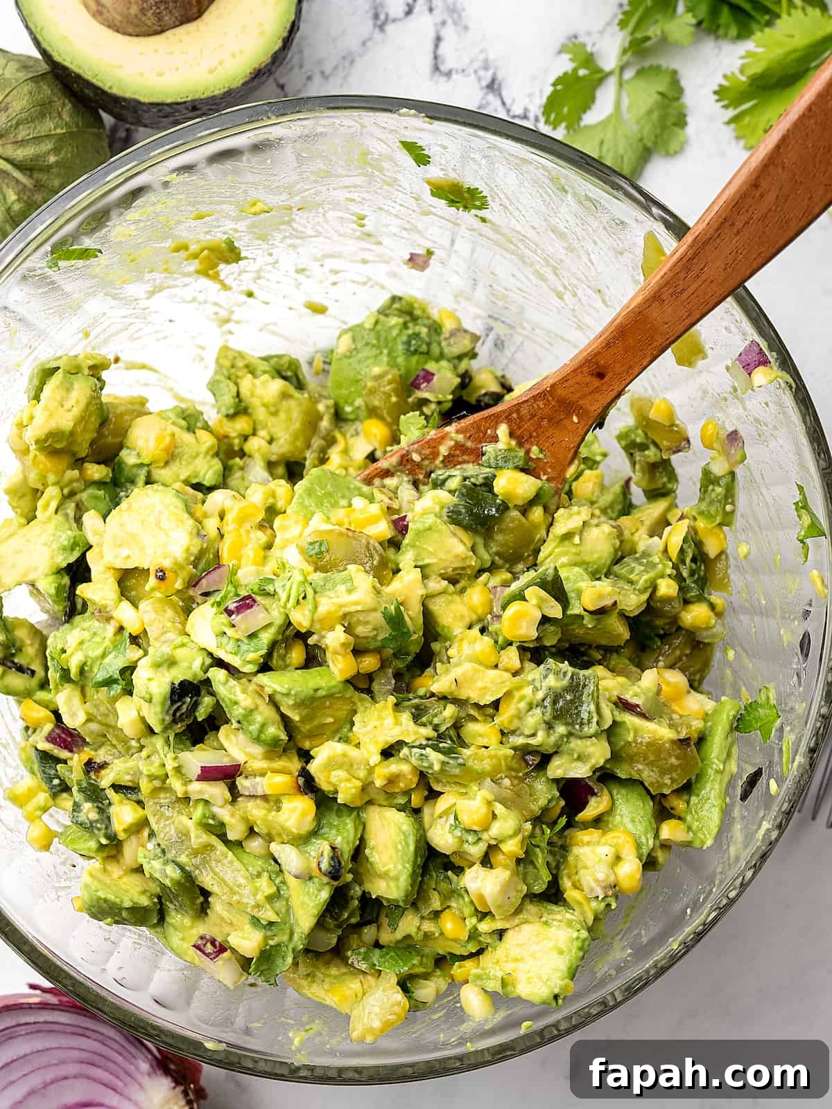 Grilled corn being mixed with avocado chunks, chopped tomatillos, green chile, red onion, cilantro and salt