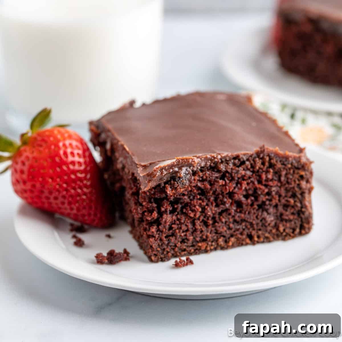 Moist Buttermilk Chocolate Cake Recipe for Rich Chocolate Flavor 2 A slice of chocolate cake on a white plate with a strawberry.