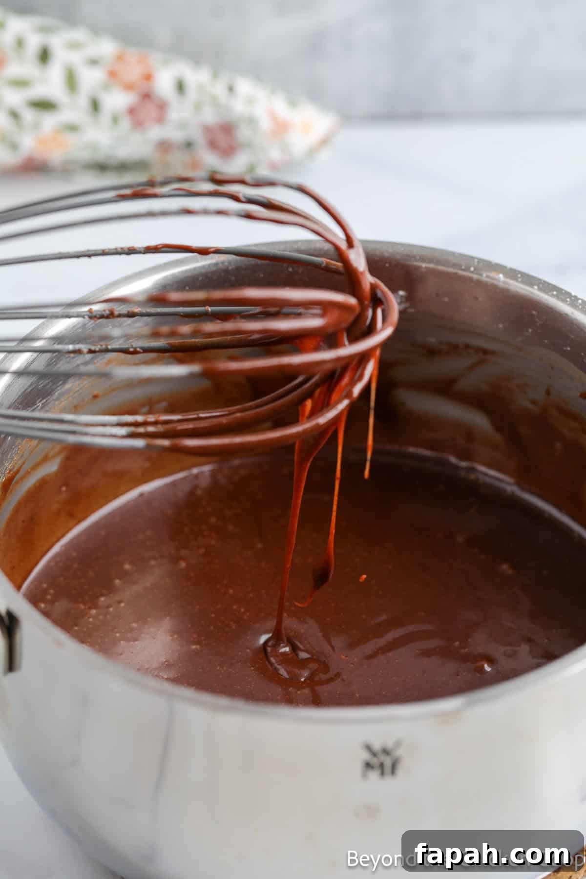 Moist Buttermilk Chocolate Cake Recipe for Rich Chocolate Flavor 10 A whisk dripping with chocolate icing.