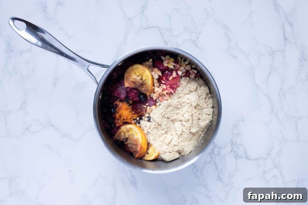 A small saucepan filled with oranges, berries, sugar and spices ready to make mulled berry jam.