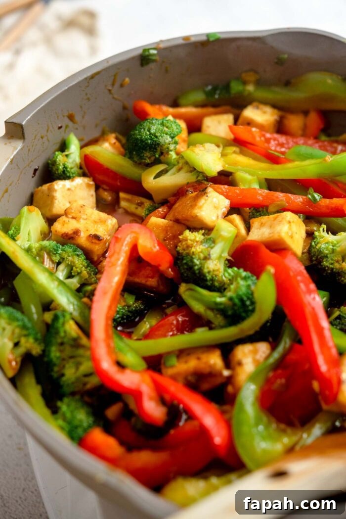 Crispy Orange Tofu Stir-Fry with Tangy Citrus Glaze 7 Cubed tofu and stir fried vegetables cooking in a stick orange sauce in a pan.