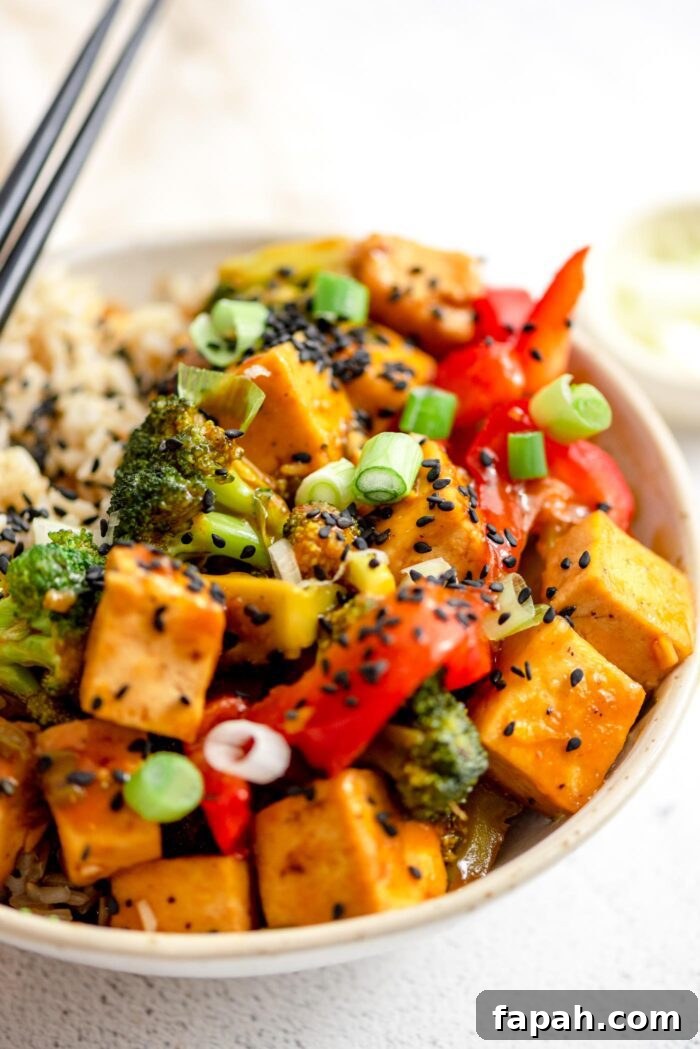 Crispy Orange Tofu Stir-Fry with Tangy Citrus Glaze 8 Close up of a bowl of orange tofu and vegetable stir fry topped with black sesame seeds.
