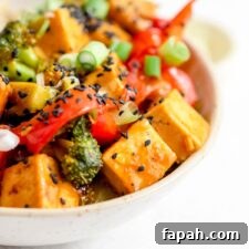 Crispy Orange Tofu Stir-Fry with Tangy Citrus Glaze 9 Pair of chopsticks rests on a bowl of stir fried vegetables and tofu in orange sauce.